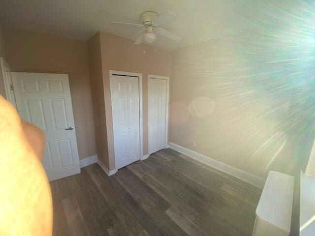 unfurnished bedroom with dark wood-type flooring, ceiling fan, and two closets