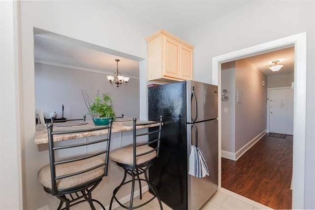 kitchen with cream cabinets, light wood-type flooring, decorative light fixtures, stainless steel refrigerator, and a chandelier