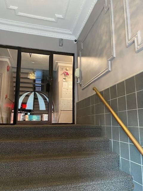 stairway featuring tile walls, tile patterned floors, and crown molding