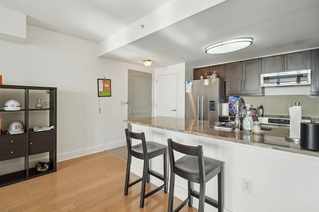 kitchen with decorative backsplash, a kitchen breakfast bar, dark brown cabinets, a peninsula, and stainless steel appliances