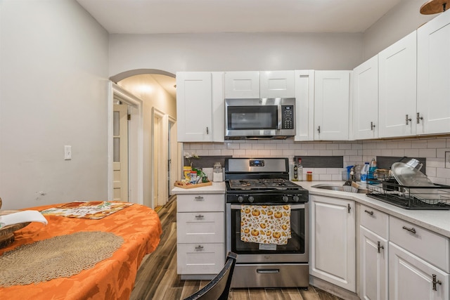 kitchen with sink, appliances with stainless steel finishes, white cabinetry, dark hardwood / wood-style floors, and tasteful backsplash