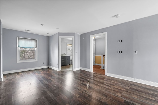 unfurnished room featuring dark wood-type flooring, a sink, visible vents, and baseboards