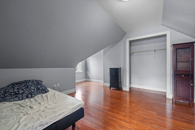 bedroom with vaulted ceiling, hardwood / wood-style floors, a closet, and baseboards