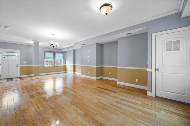 empty room featuring ornamental molding, visible vents, light wood finished floors, and an inviting chandelier