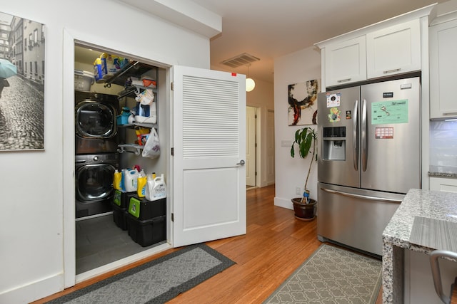 kitchen with white cabinets, stacked washer / drying machine, light wood-style flooring, stainless steel refrigerator with ice dispenser, and visible vents