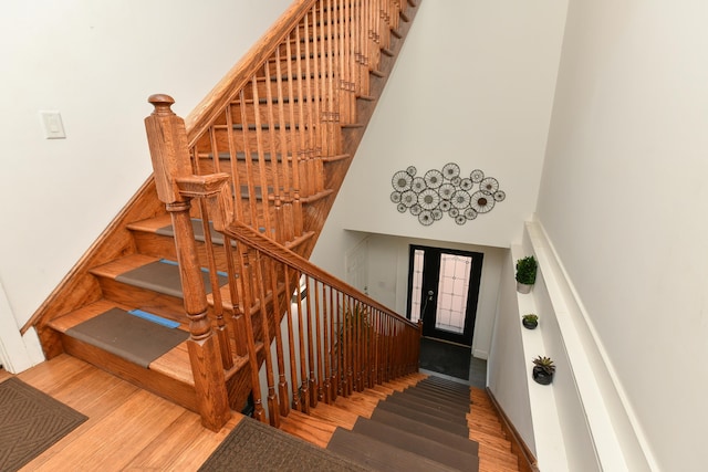 staircase featuring baseboards, a high ceiling, and wood finished floors
