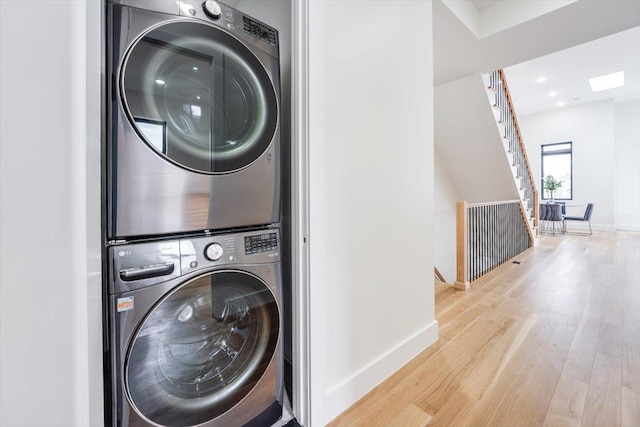 laundry room featuring baseboards, wood finished floors, laundry area, and stacked washing maching and dryer