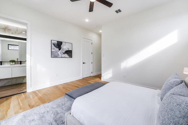 bedroom with wood finished floors, visible vents, ensuite bathroom, and baseboards