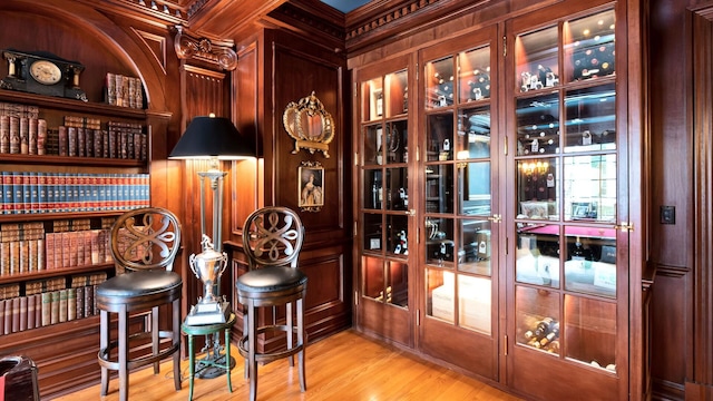 wine area with built in features, wooden walls, crown molding, and light hardwood / wood-style flooring