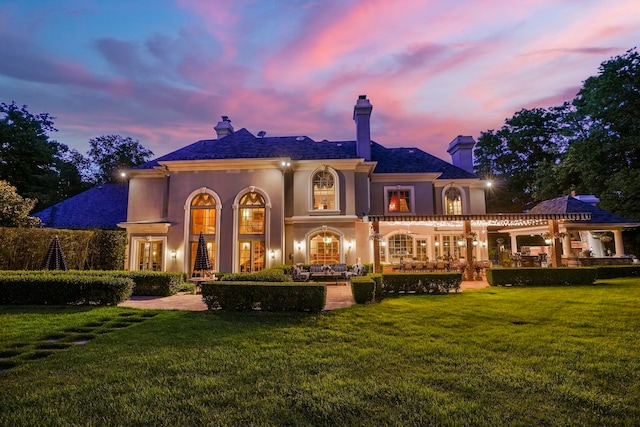 back house at dusk featuring a lawn