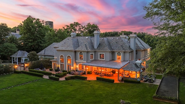 back house at dusk with an outdoor hangout area, a patio area, and a lawn