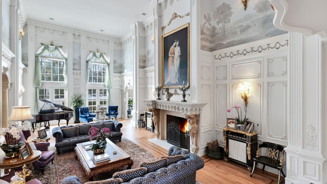 living room with light wood-type flooring, a high end fireplace, ornamental molding, and a towering ceiling