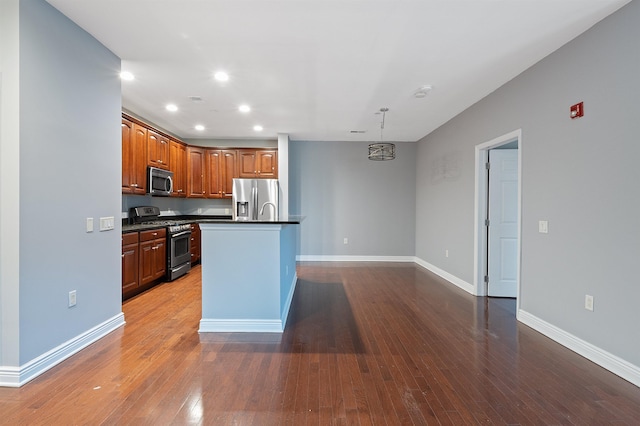 kitchen featuring dark hardwood / wood-style flooring, stainless steel appliances, decorative light fixtures, and an island with sink