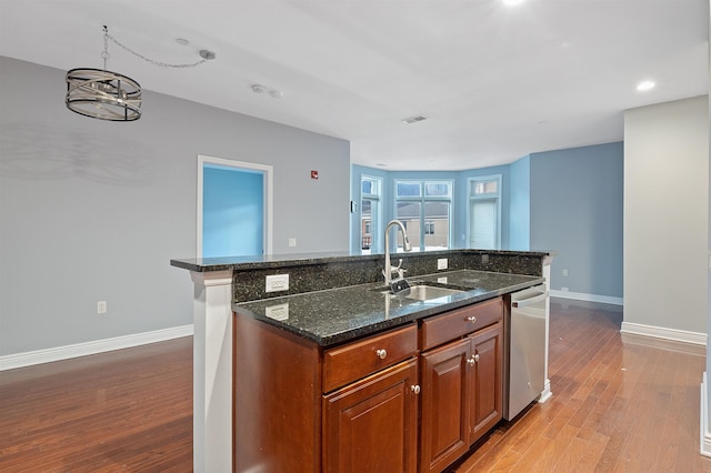 kitchen featuring sink, dishwasher, dark stone countertops, light wood-type flooring, and a kitchen island with sink