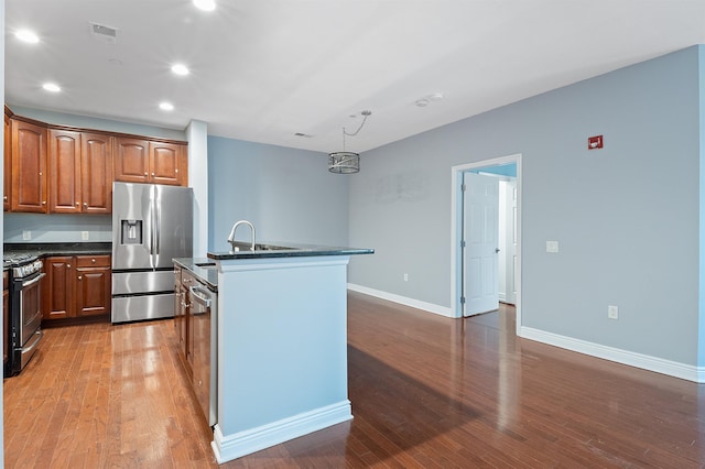 kitchen with a kitchen island with sink, appliances with stainless steel finishes, pendant lighting, sink, and light hardwood / wood-style flooring