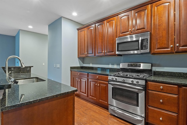 kitchen with stainless steel appliances, dark stone countertops, light hardwood / wood-style flooring, and sink