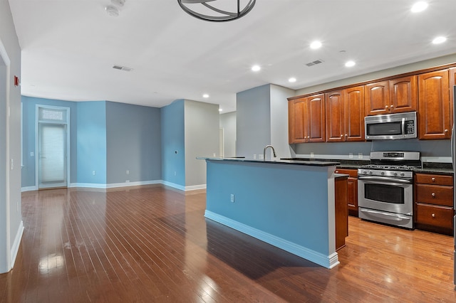 kitchen with sink, stainless steel appliances, an island with sink, and hardwood / wood-style flooring