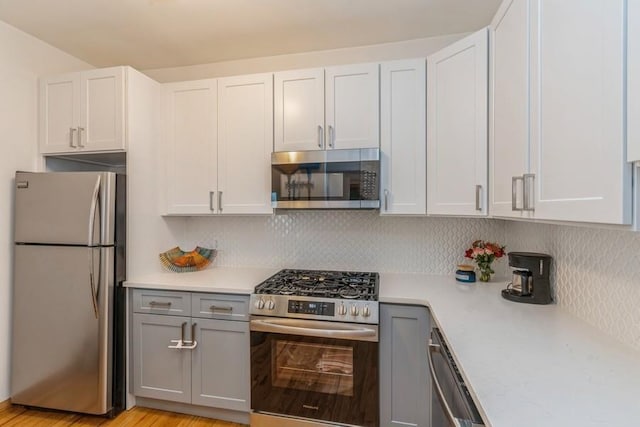 kitchen with backsplash, appliances with stainless steel finishes, white cabinetry, and gray cabinetry