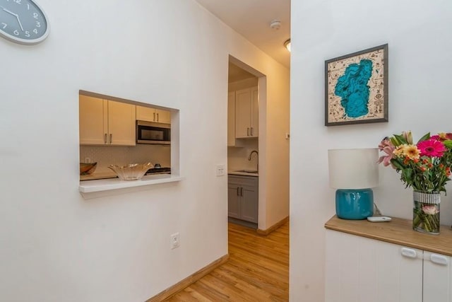 hall featuring a sink, light wood-type flooring, and baseboards