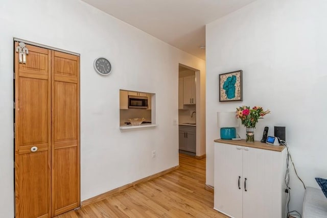 corridor featuring baseboards, light wood-type flooring, and a sink