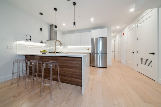 kitchen with white cabinets, sink, backsplash, stainless steel refrigerator, and light wood-type flooring