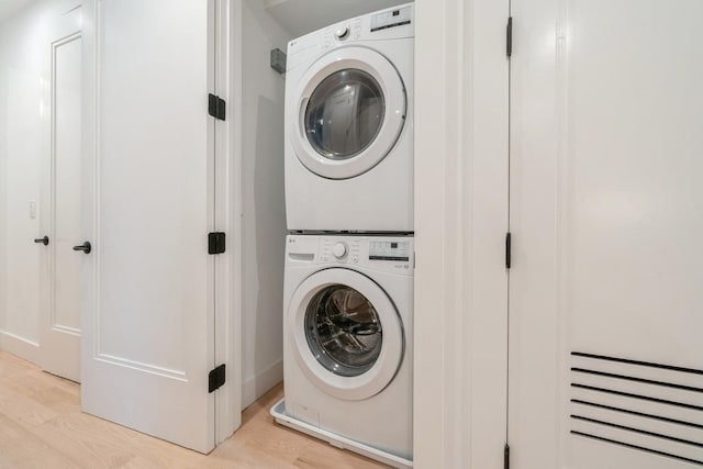 clothes washing area with light wood-type flooring and stacked washer / drying machine