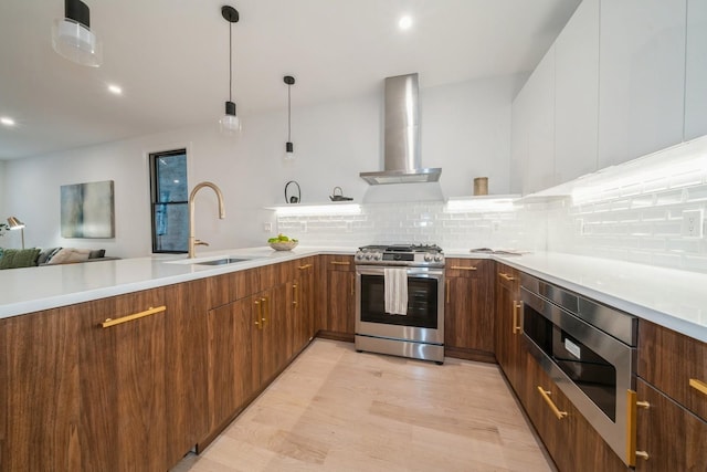 kitchen featuring wall chimney exhaust hood, tasteful backsplash, stainless steel gas stove, sink, and hanging light fixtures