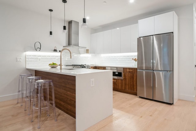 kitchen featuring appliances with stainless steel finishes, hanging light fixtures, white cabinets, kitchen peninsula, and wall chimney exhaust hood