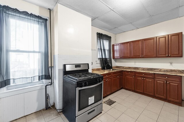 kitchen with a paneled ceiling, gas range, light tile patterned floors, sink, and light stone countertops