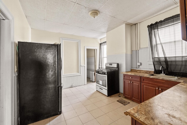 kitchen featuring black fridge, sink, gas stove, and light tile patterned floors