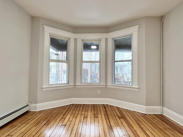 unfurnished room featuring a wealth of natural light, light hardwood / wood-style flooring, and baseboard heating