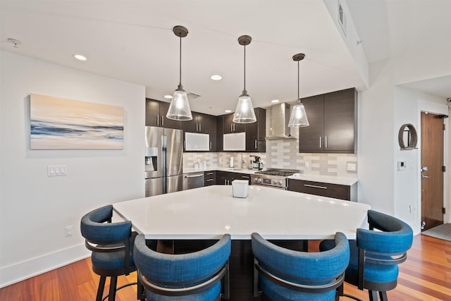 84 Willow Ave Unit 4B, Hoboken, NJ 07030 - kitchen with appliances with stainless steel finishes, wall chimney range hood, a kitchen breakfast bar, light countertops, and light wood-style floors
