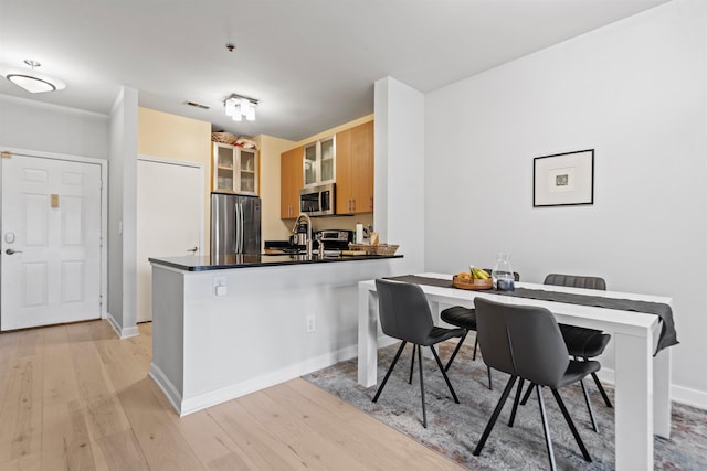24 Ave At Port Imperial Unit 305, West New York, NJ 07093 - kitchen featuring dark countertops, glass insert cabinets, stainless steel appliances, light wood finished floors, and a peninsula