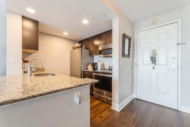 kitchen featuring stainless steel appliances, a sink, dark wood-style floors, dark brown cabinetry, and light stone counters