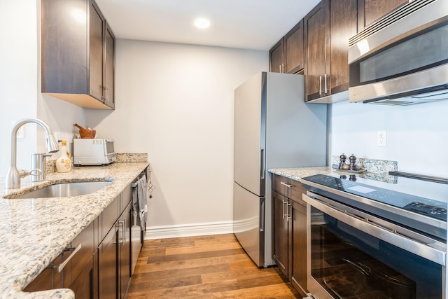 kitchen featuring appliances with stainless steel finishes, a sink, dark brown cabinets, light wood-type flooring, and recessed lighting