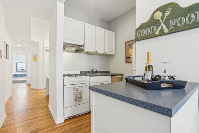 kitchen with dark countertops, under cabinet range hood, white range with gas cooktop, white cabinetry, and a sink