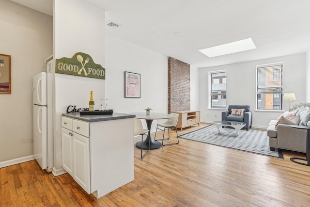 kitchen with visible vents, light wood finished floors, a skylight, white cabinetry, and open floor plan