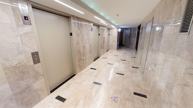 hallway with visible vents, tile walls, and elevator