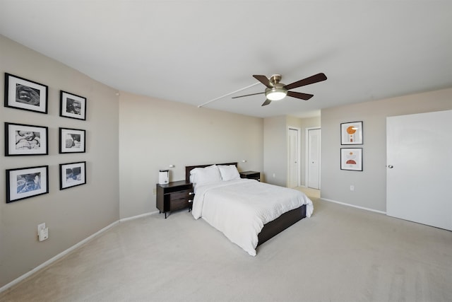 bedroom featuring light carpet, baseboards, a ceiling fan, and multiple closets