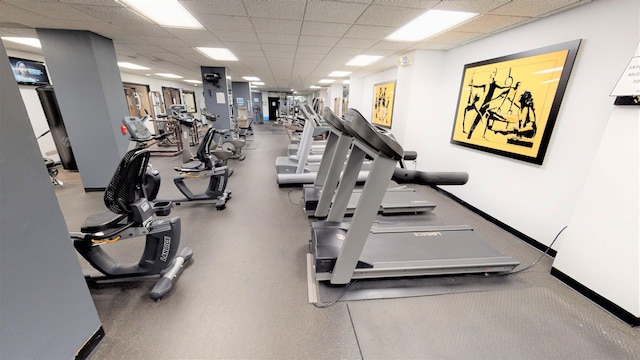 gym featuring a paneled ceiling and baseboards