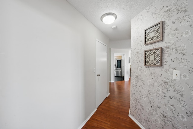 hallway with wallpapered walls, a textured ceiling, baseboards, and wood finished floors