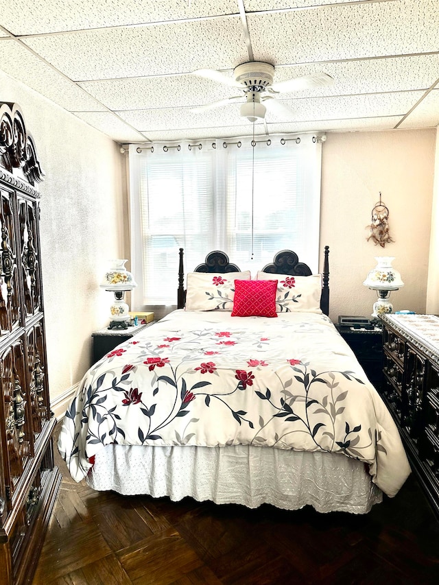 bedroom with parquet floors, a drop ceiling, and ceiling fan