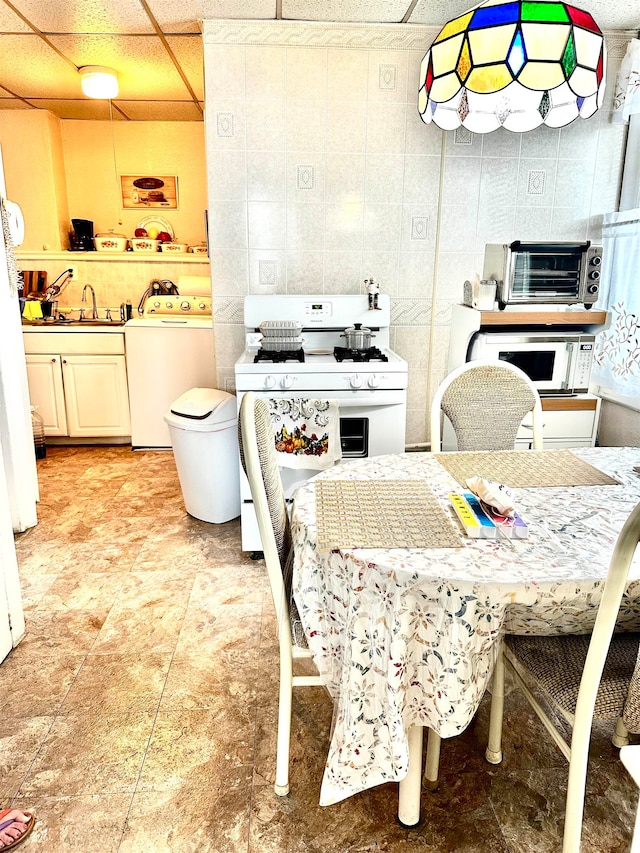 kitchen featuring tile walls, a paneled ceiling, washer / clothes dryer, sink, and white appliances