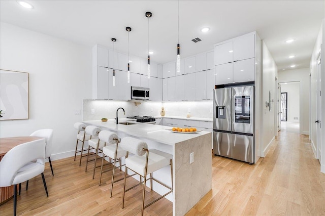 kitchen with kitchen peninsula, pendant lighting, appliances with stainless steel finishes, sink, and white cabinets