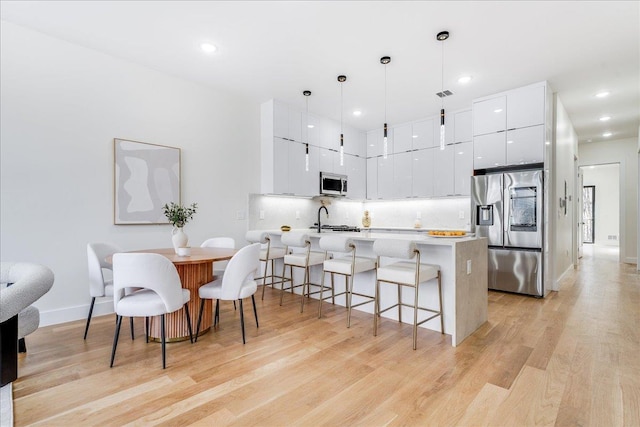 kitchen with white cabinetry, a kitchen breakfast bar, light hardwood / wood-style flooring, pendant lighting, and stainless steel appliances