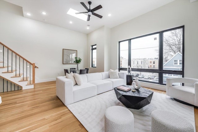 living room with a skylight, ceiling fan, light hardwood / wood-style flooring, and a towering ceiling