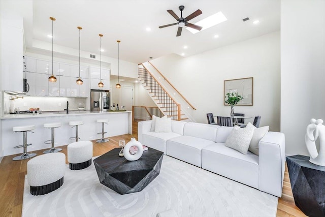 living room featuring ceiling fan, light hardwood / wood-style floors, sink, and a skylight