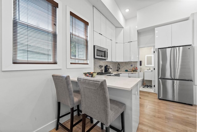 35 Manhattan Ave Unit 4, Jersey City, NJ 07307 - kitchen featuring appliances with stainless steel finishes, a peninsula, a kitchen breakfast bar, white cabinetry, and backsplash