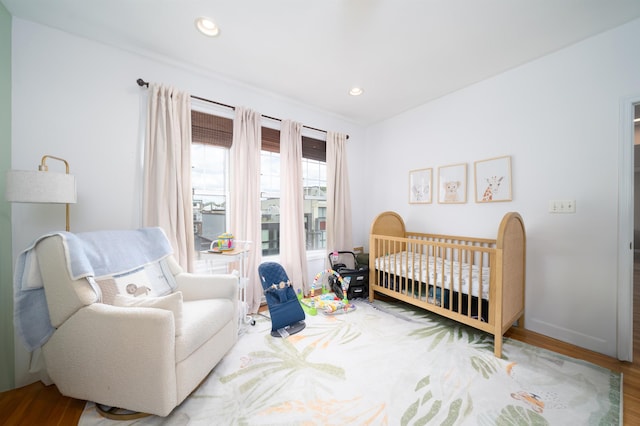 bedroom featuring recessed lighting, baseboards, a crib, and wood finished floors