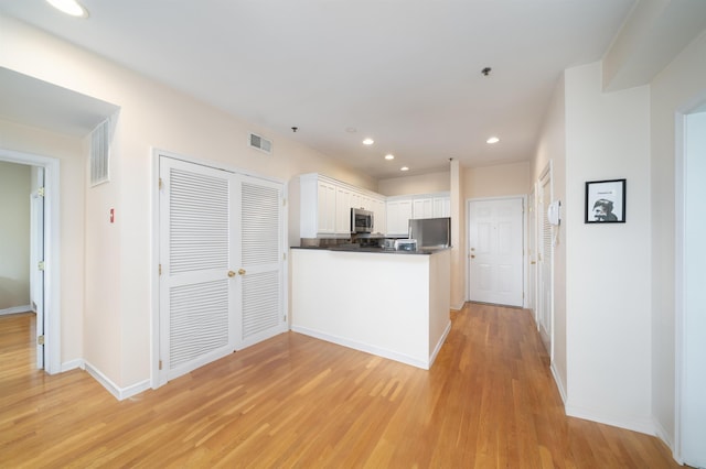 kitchen featuring stainless steel appliances, a peninsula, light wood-style flooring, and white cabinetry